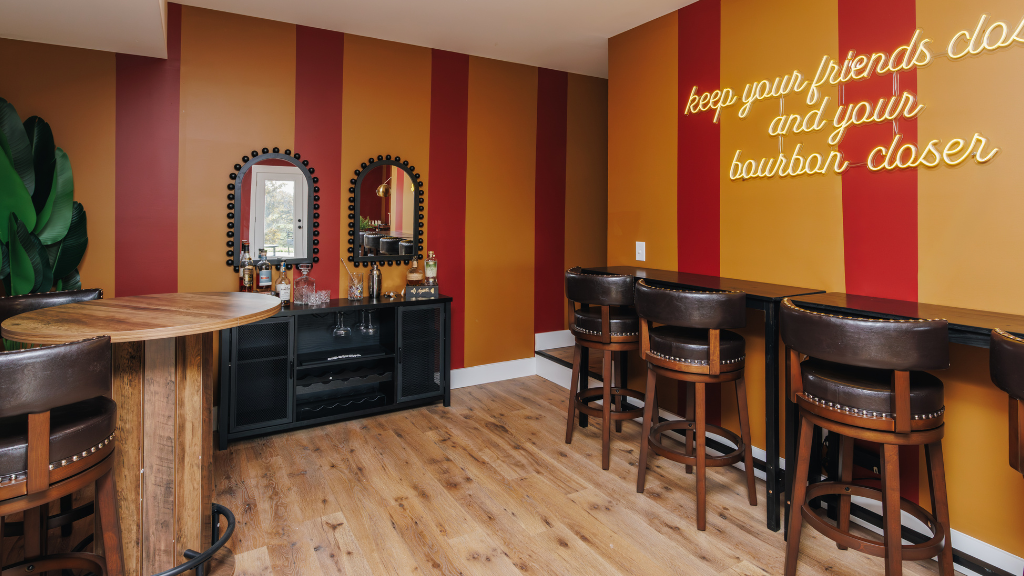 Airbnb bar area with striped walls and a neon sign, featuring wooden flooring and bar stools.